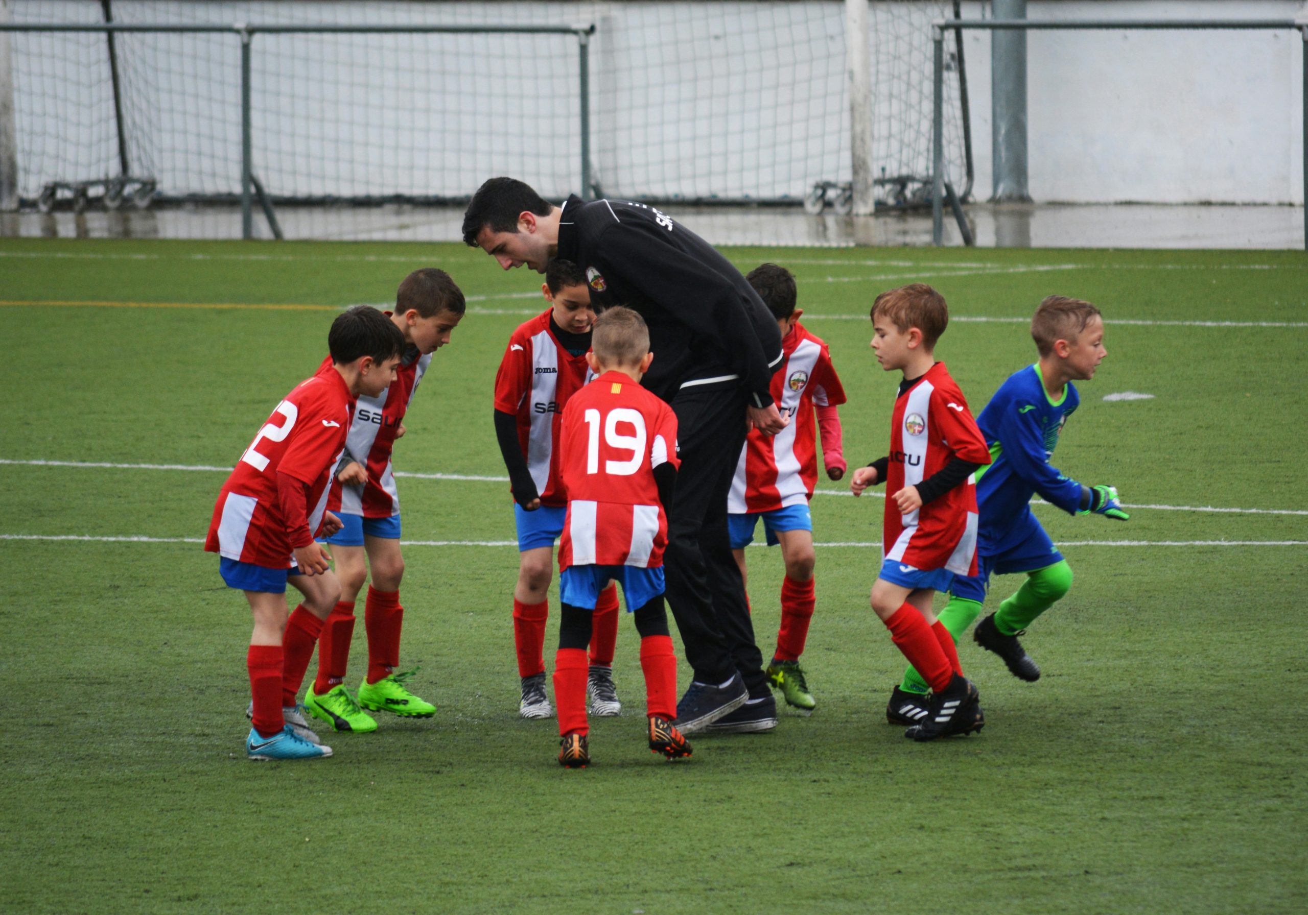 Adult coach dressed in black on the pitch with a youth soccer team in red uniforms