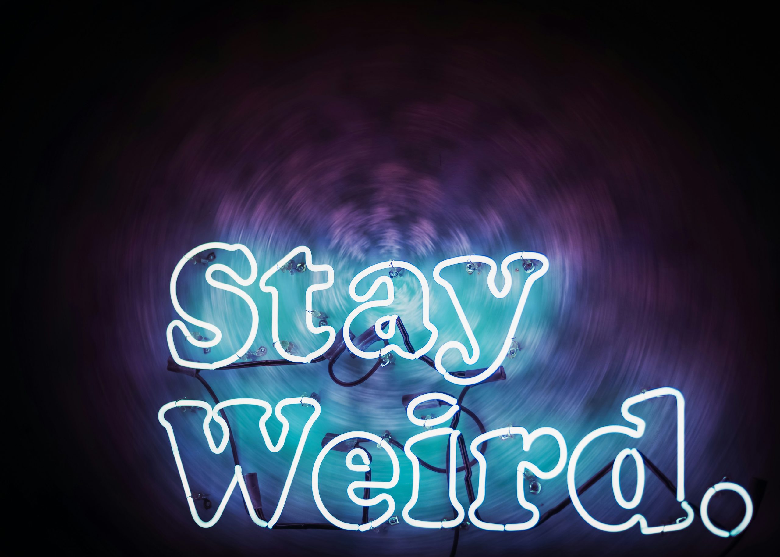 Blue neon "Stay Weird." sign against a dark background