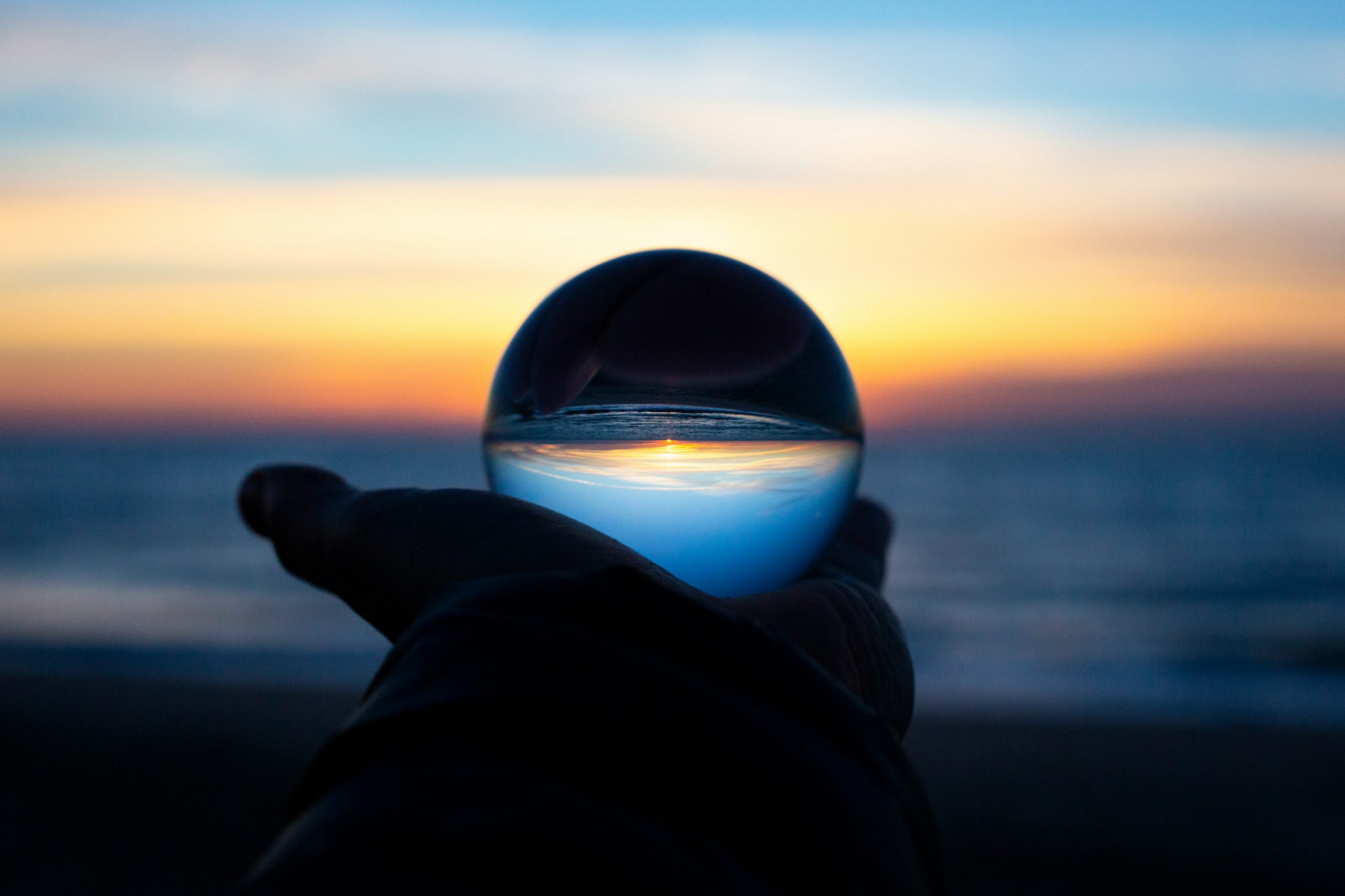 hand holding a crystal ball up to a sunrise, showing a reverse image within