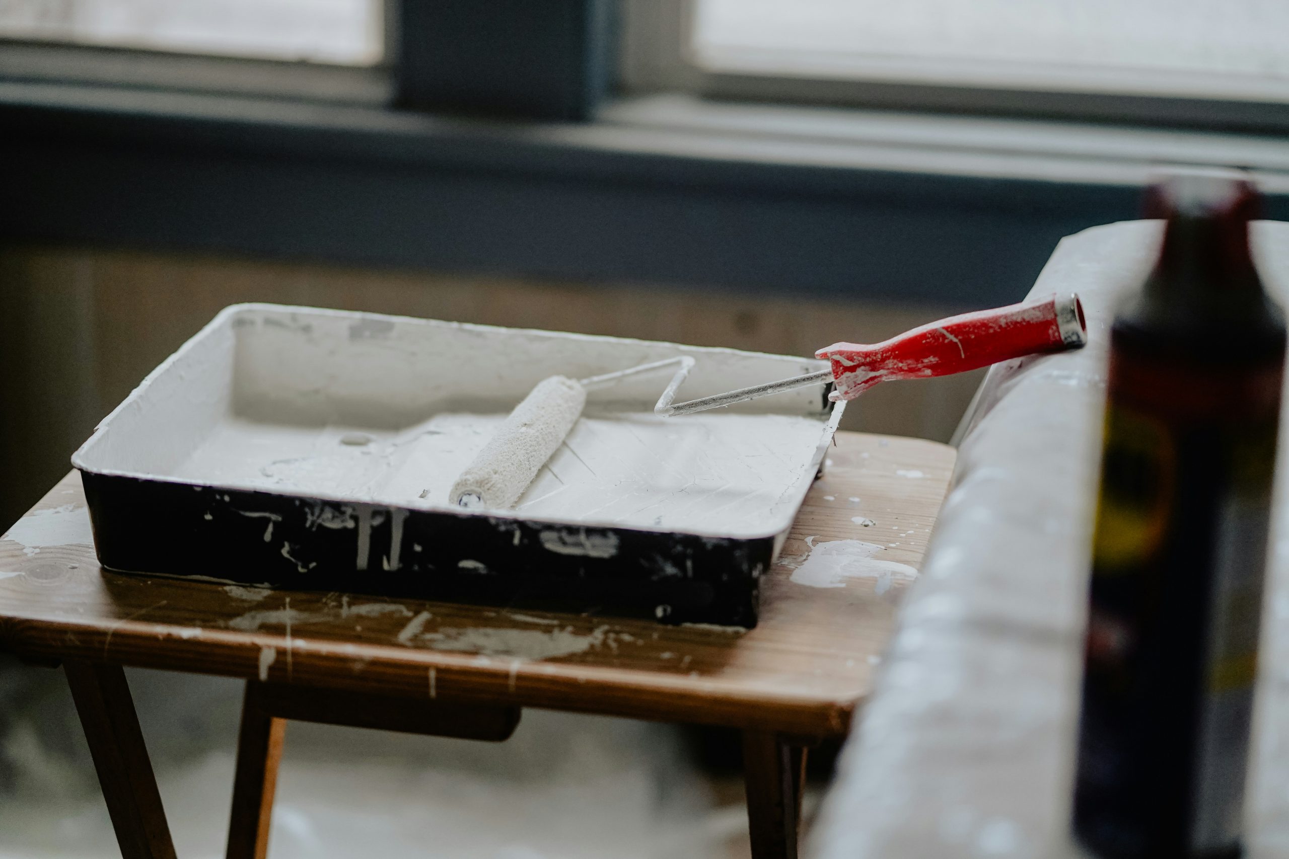 painting tray with white paint and a roller brush on a brown wooden table