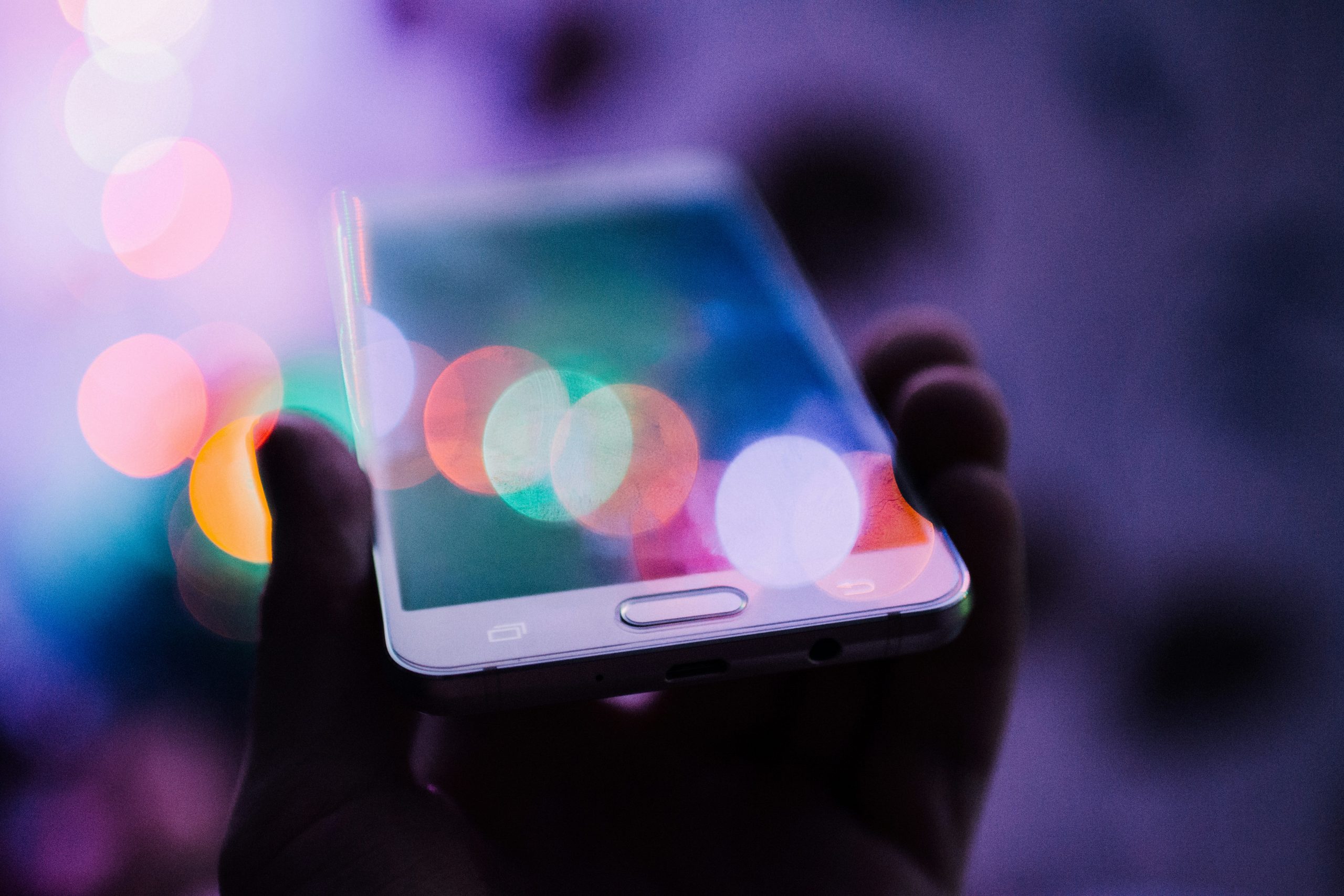 Hand holding a smart phone against a sparkly purple background