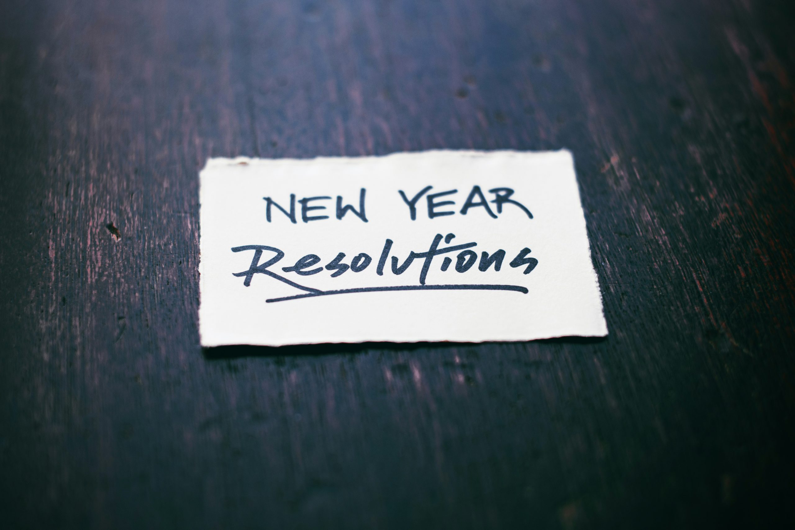 White paper with New Year Resolutions written on it in black ink against a dark brown stained wood background